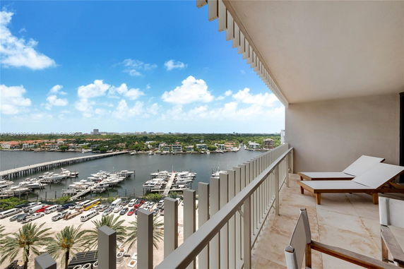 Panoramic view from a balcony showing a marina with boats and distant buildings under a blue sky.