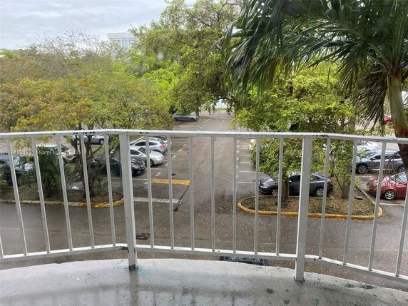 View from a balcony showing a parking lot with several cars and surrounding trees.