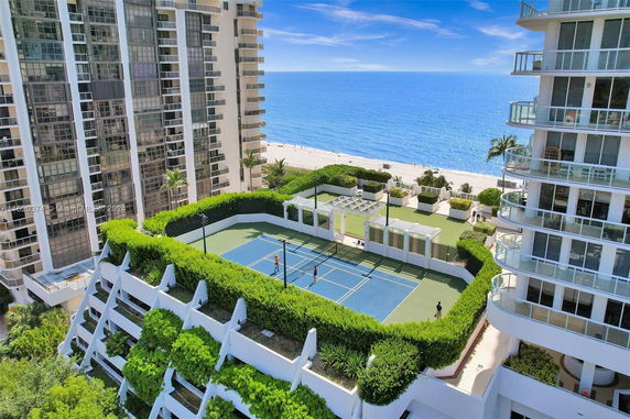 Rooftop tennis court with surrounding greenery on a high-rise building near the beach.