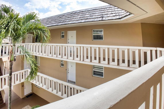 Exterior view of multi-story building with open corridors and palm tree.