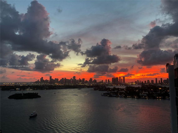 Wide angle view of a city skyline at sunset with a water body in the foreground.