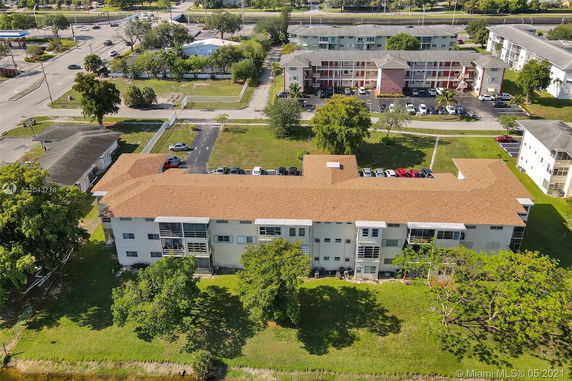 Aerial view of a multi-story building with a tan roof situated in a residential area.