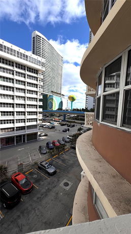 View of a parking area below tall buildings with a variety of parked cars.