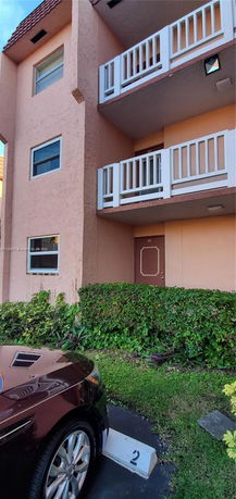 Front view of a multi-story building with balconies and parking space.