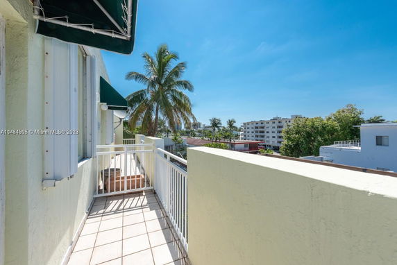 Balcony view overlooking residential buildings and palm trees under a clear blue sky.