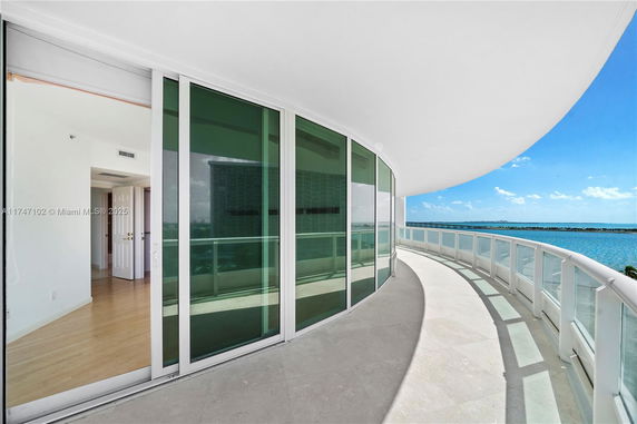 Curved balcony with glass railings overlooking a water body under a clear blue sky.