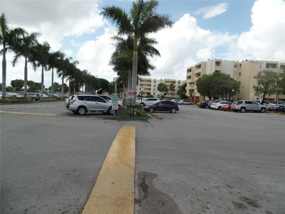 View of a parking lot with multiple cars and apartment buildings in the background.