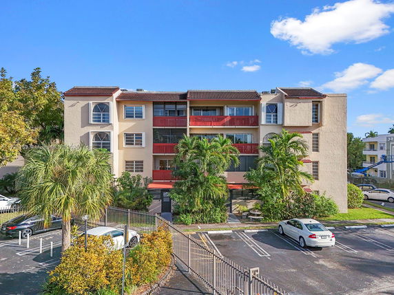 Front view of a multi-story residential building with balconies and parking area in front.