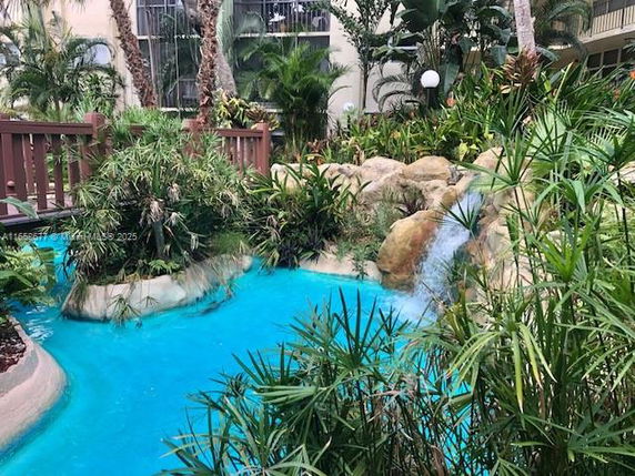 Outdoor area with a rock waterfall and blue water surrounded by lush greenery.