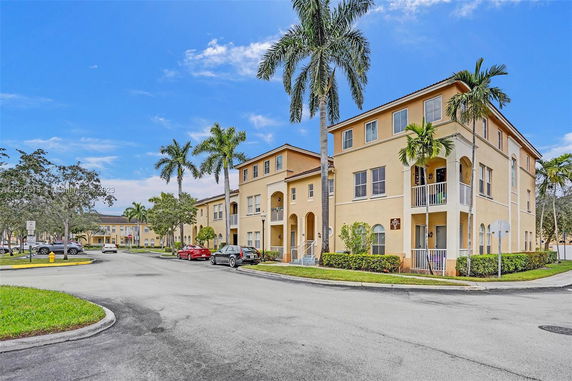 Front view of a multi-story residential building with balconies and palm trees.