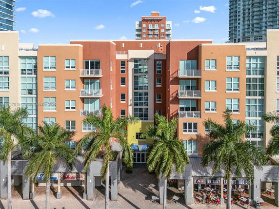 Front view of a multi-story residential building with balconies and palm trees.