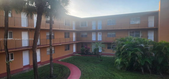 View of a multi-story apartment building with exterior corridors and a landscaped courtyard.