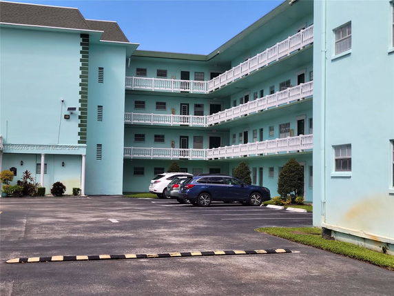 Parking area in front of a multi-story building with balconies.
