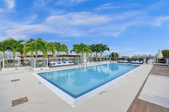 Outdoor swimming pool area with lounge chairs and palm trees.