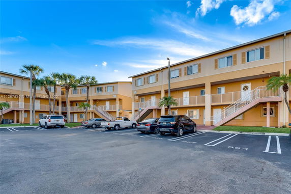 Front view of a three-story apartment complex with external staircases and parking spaces.