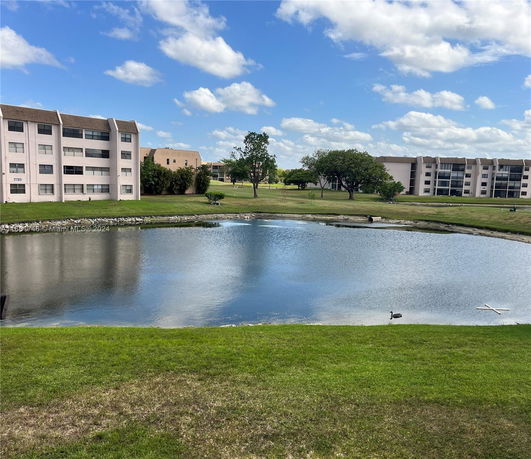 Buildings surrounding a pond with grassy areas and trees.