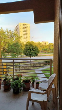 View from a balcony overlooking a road, trees, and a tall building.