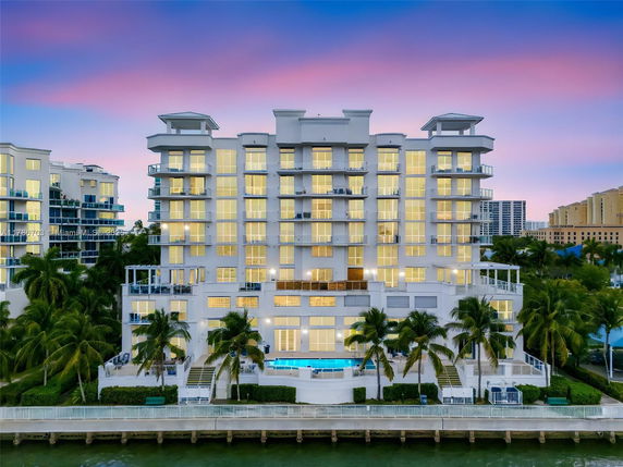 Front view of a multi-story building with balconies and large windows, set against a twilight sky.