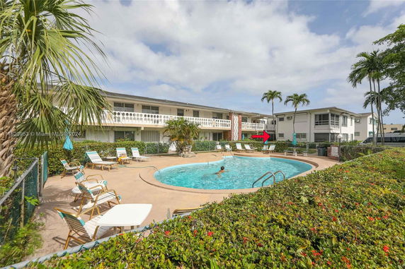 Outdoor view of a swimming pool area with a two-story residential building in the background.