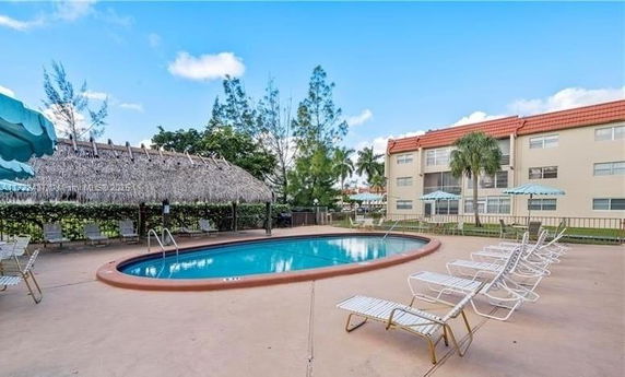 Outdoor swimming pool with surrounding lounge chairs and a thatched shade structure.