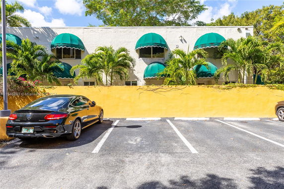 Outdoor parking area with cars and a building with green awnings.