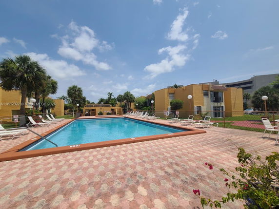 Outdoor swimming pool with surrounding lounge chairs and nearby buildings.