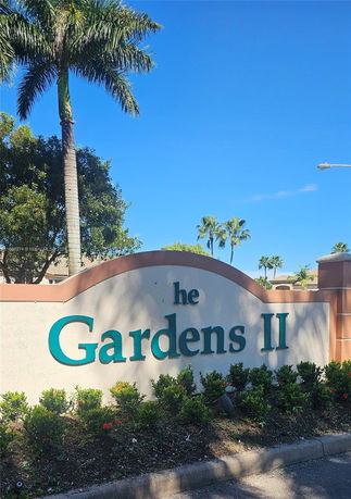 Sign with the text 'Gardens II' surrounded by plants and trees.