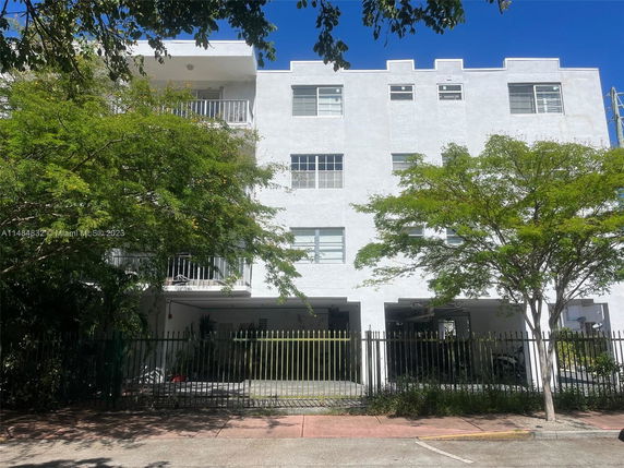 Front view of a multi-story white building with balconies and a fenced entrance.