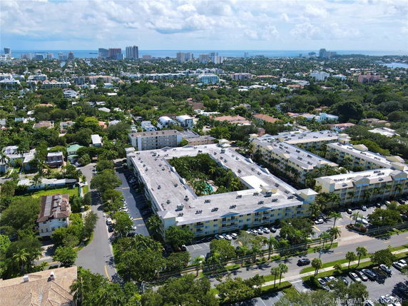 Panoramic view of a residential area with multiple buildings and surrounding greenery, with cityscape and ocean in the distance.