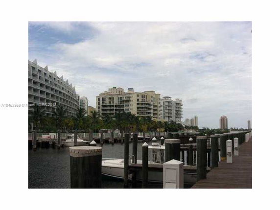 View of high-rise buildings near a waterfront with a dock and boats in the foreground.