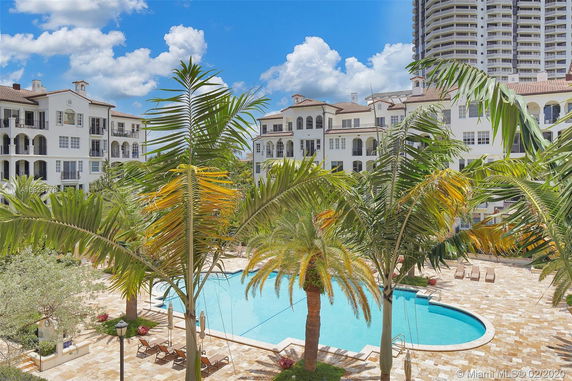 Outdoor view of a swimming pool surrounded by palm trees and multi-story buildings.