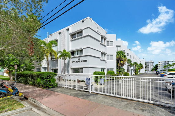 Front view of a multi-story white building with gated entrance and parking area.