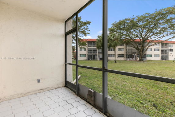 View from a screened porch overlooking a grassy area and apartment buildings.