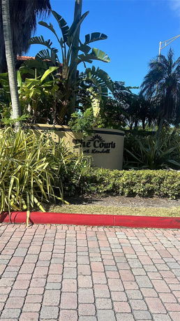 Entrance sign with landscaping and palm trees.
