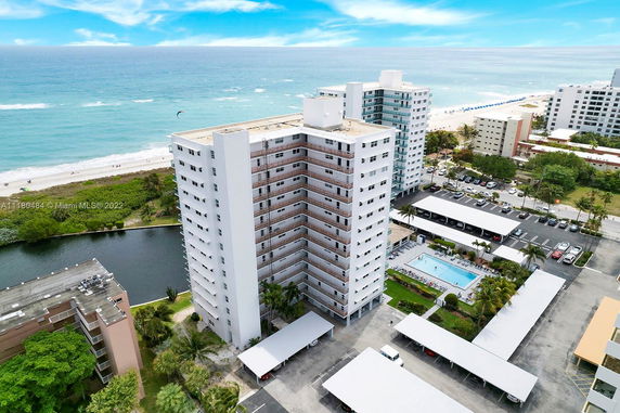 Aerial view of a high-rise building near the beach with a swimming pool and parking area.