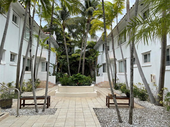 View of a landscaped courtyard between two white two-story buildings with palm trees.