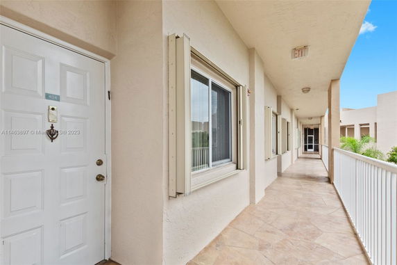 Long exterior corridor in a residential building with doors and windows.