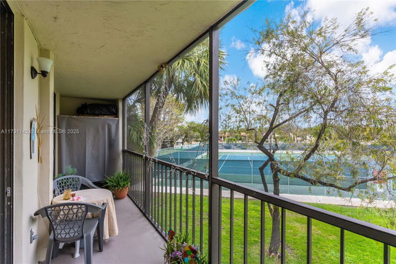 Outdoor view from a balcony overlooking tennis courts and trees.
