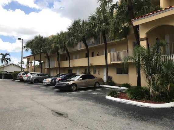 Outdoor parking area in front of a multi-story building with palm trees.