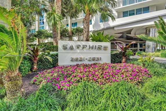 Front view of a building entrance with a sign reading 'Sapphire' surrounded by plants.