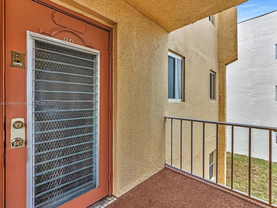 Exterior view of an apartment entrance with a metal door and railing on a small balcony.