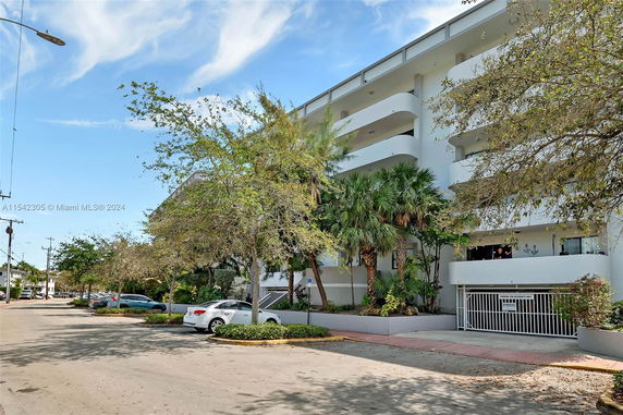Front view of a multi-story building with balconies and tropical landscaping.