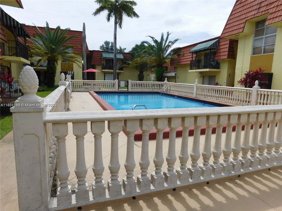 Outdoor swimming pool surrounded by a white balustrade and palm trees.