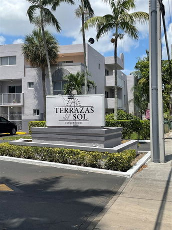 Front view of a condominium complex with palm trees and a sign reading 'Terrazas del Sol Condominiums.'