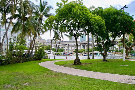 View of a waterfront area with trees and a walkway, overlooking a bridge and cityscape.