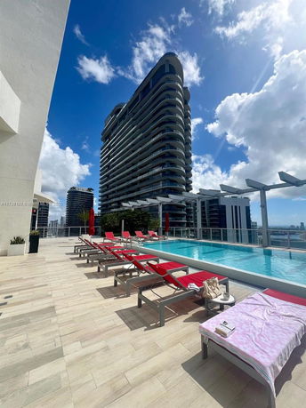 Rooftop swimming pool with lounge chairs and a view of a modern high-rise building.