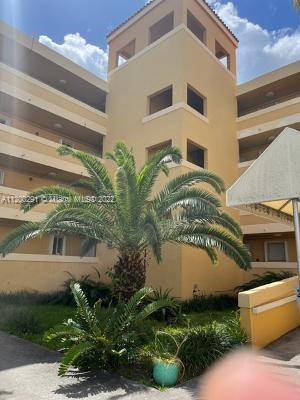 Front view of a multi-story beige building with balconies and palm tree in front.