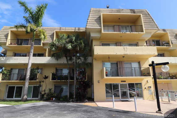 Front view of a multi-story apartment building with balconies and palm trees.