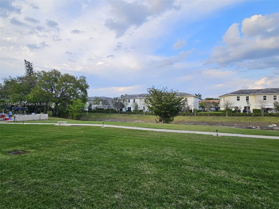 View of a grassy area with a path and residential buildings in the background.