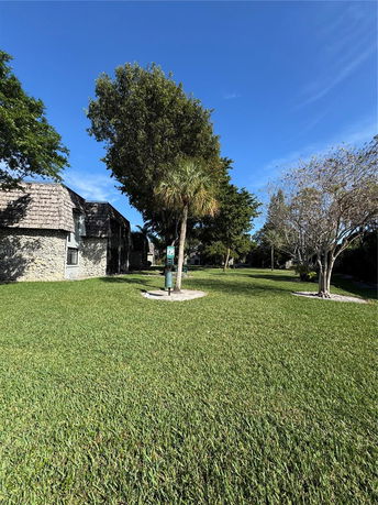 View of a building with a shingle roof and a surrounding grassy area with trees.